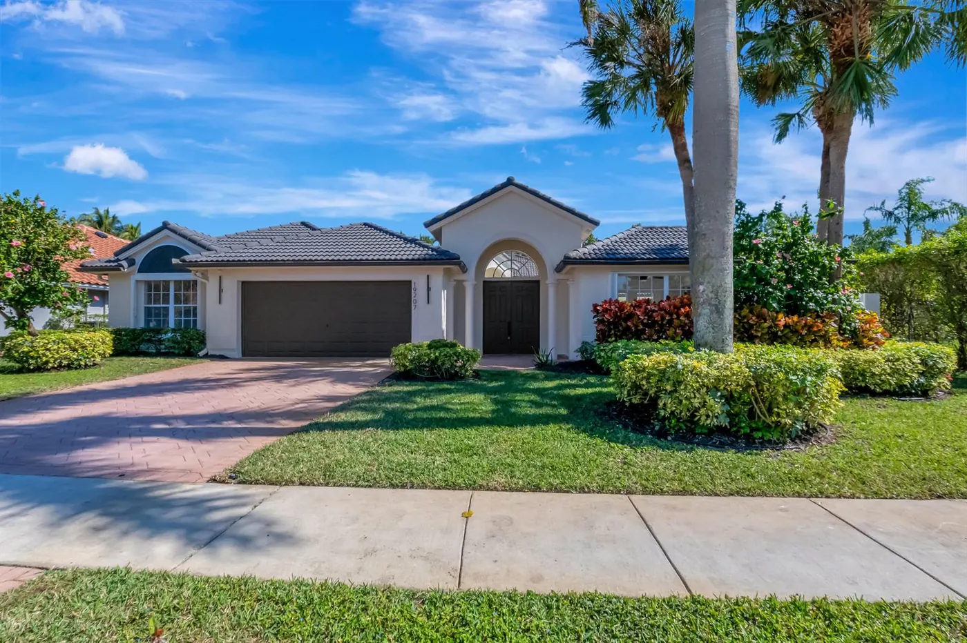 Single-story home with a tile roof, palms and a manicured lawn